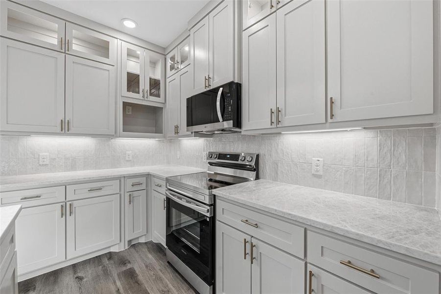 Kitchen featuring electric range, glass insert cabinets, light wood-type flooring, light stone counters, and backsplash
