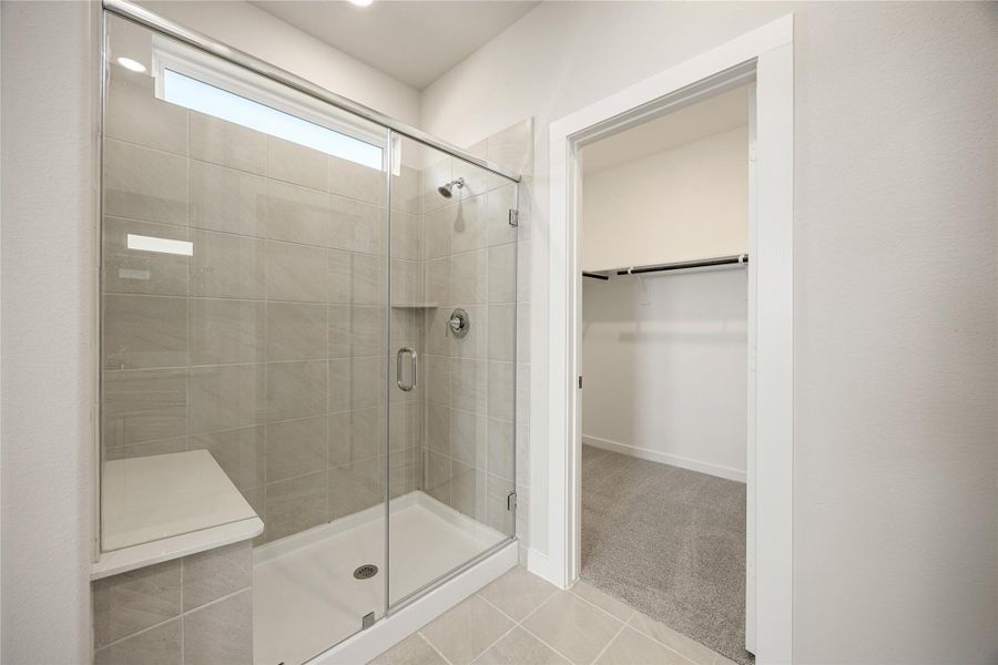 This modern primary bath features a spacious walk-in shower with elegant tile surround and glass enclosure, seamlessly connecting to the large walk-in closet for added convenience.