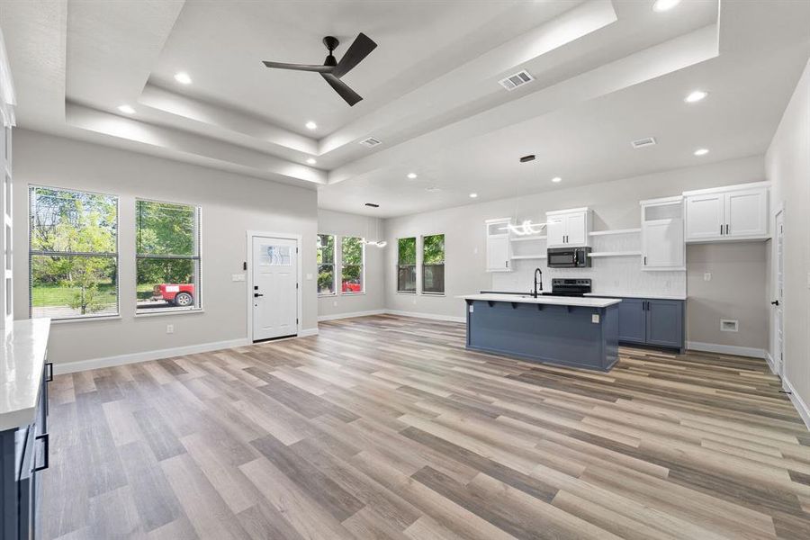 Kitchen with white cabinets, a raised ceiling, hanging light fixtures, a kitchen island with sink, and a breakfast bar