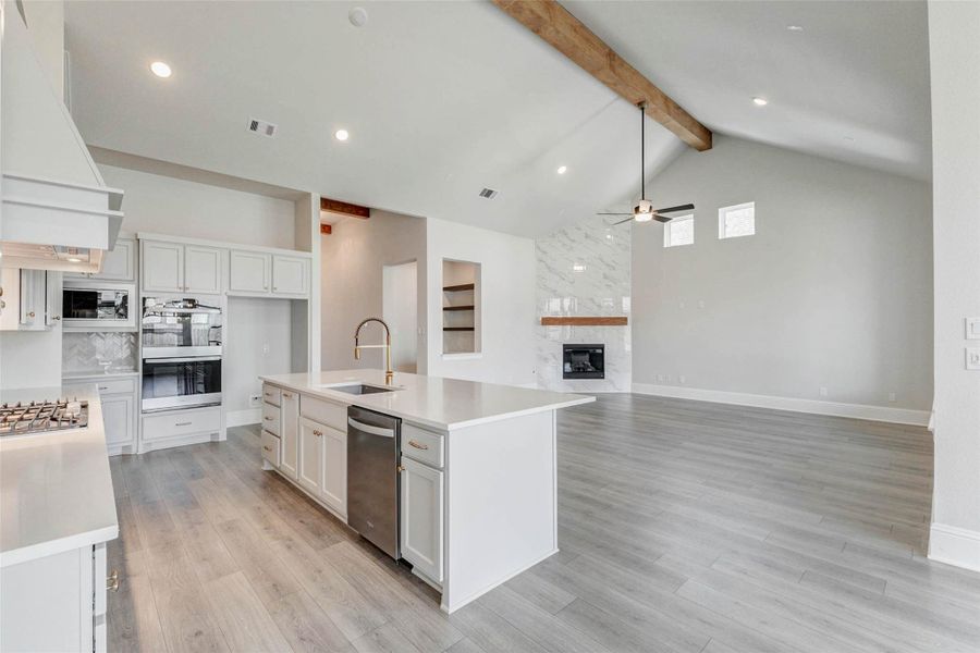 Kitchen flows into a bright living room with high ceilings, exposed beam, a ceiling fan, and a stylish fireplace, perfect for entertaining.