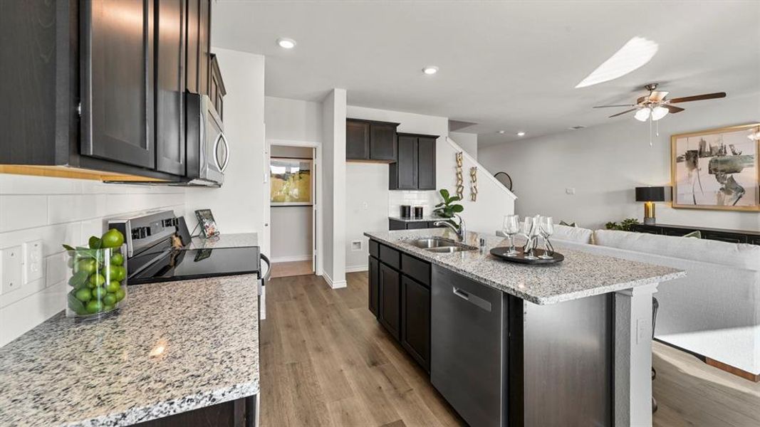 Kitchen with backsplash, light stone countertops, open floor plan, appliances with stainless steel finishes, and an island with sink