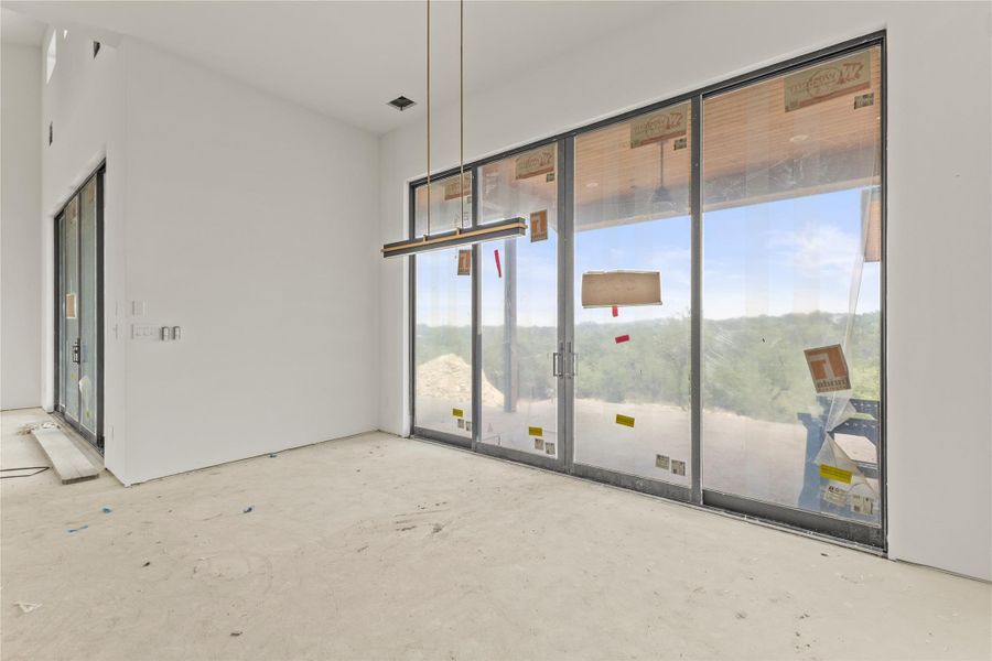 Spacious interior featuring expansive sliding glass doors, a contemporary linear pendant light fixture, high ceilings, and a secondary glass door