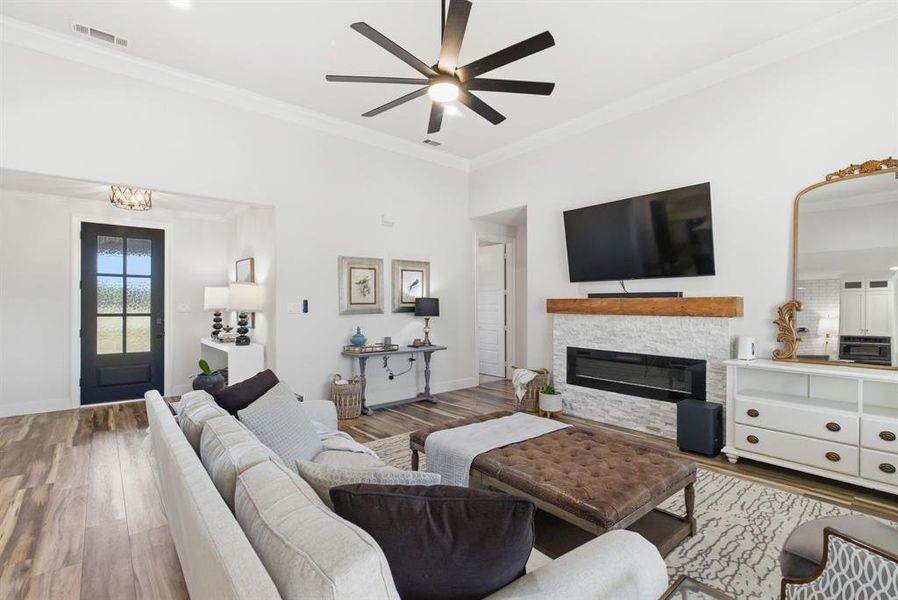 Living room with ornamental molding, a fireplace, wood finished floors, and ceiling fan