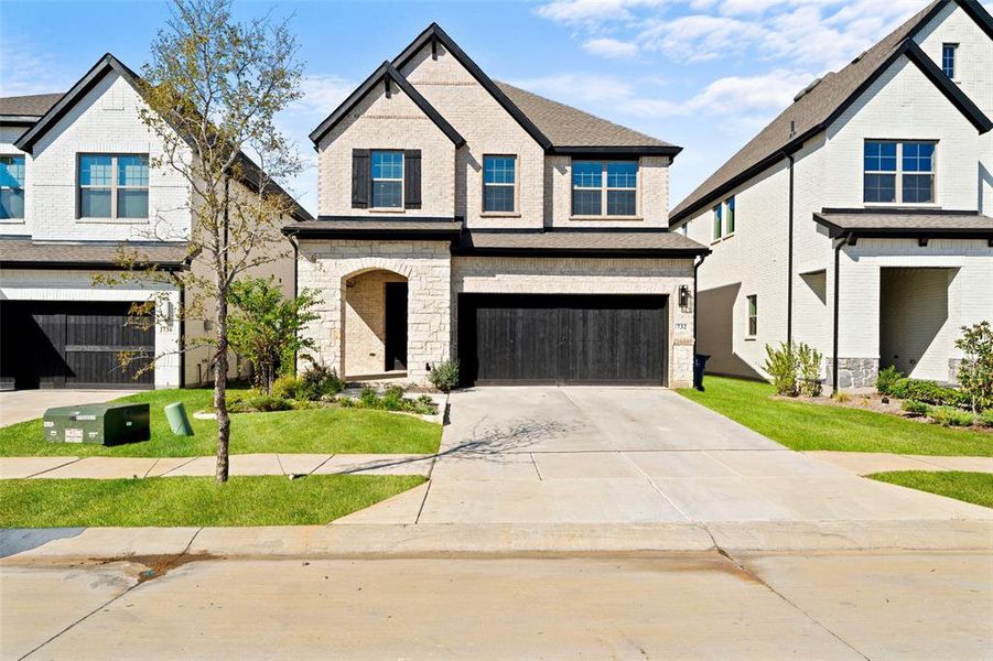 View of front of property featuring concrete driveway, stone siding, a garage, brick siding, and a front lawn View of front of property featuring concrete driveway, stone siding, a garage, brick siding, and a front lawn