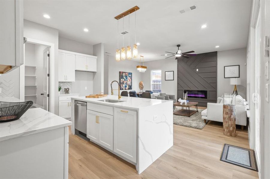 Kitchen with sink, dishwasher, white cabinetry, hanging light fixtures, and a center island with sink