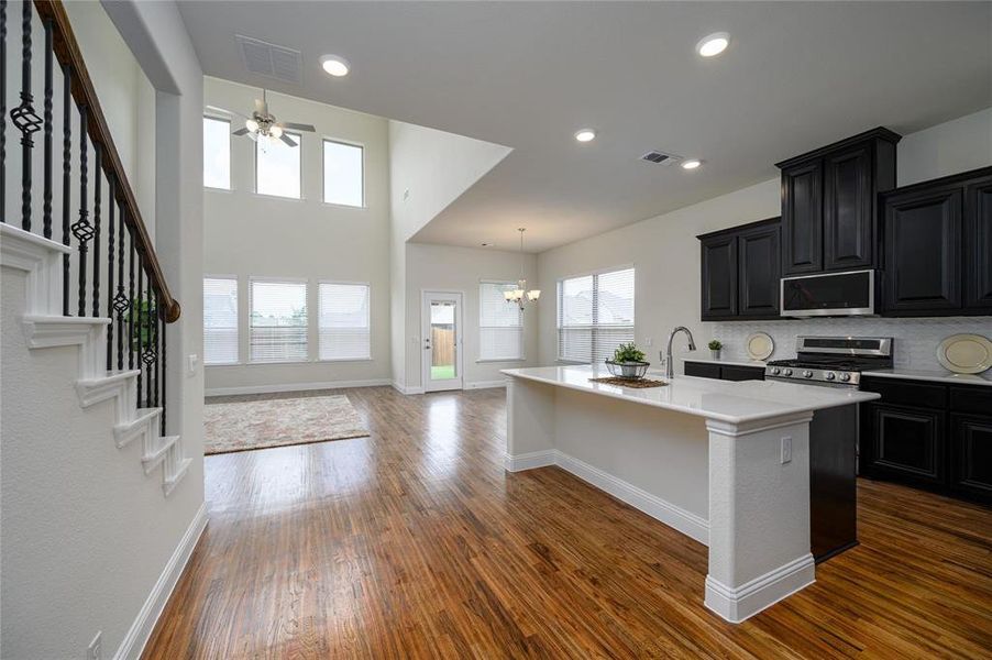 Kitchen with backsplash, dark hardwood / wood-style flooring, a kitchen island with sink, stainless steel appliances, and decorative light fixtures