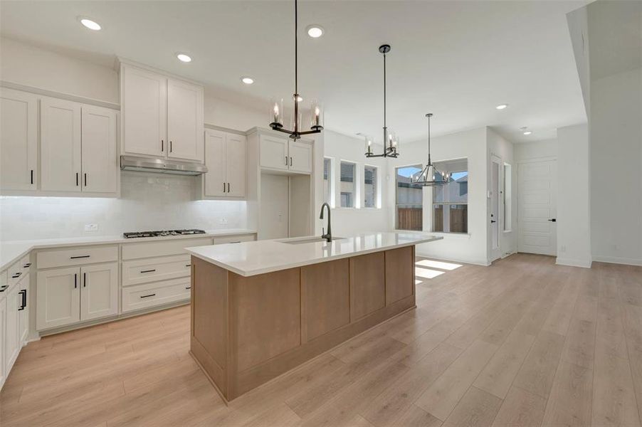 Contemporary kitchen featuring a large island with a light wood base, white countertops, and white shaker-style cabinetry with matte black hardware Contemporary kitchen featuring a large island with a light wood base, white countertops, and white shaker-style cabinetry with matte black hardware