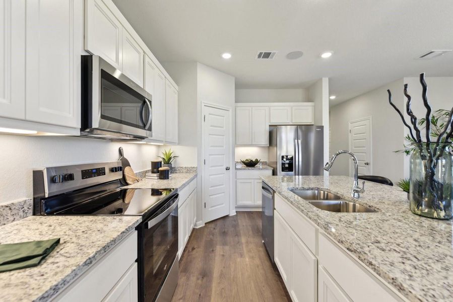 Polished granite countertops and classic white cabinetry frame this open kitchen space with wood-style flooring.