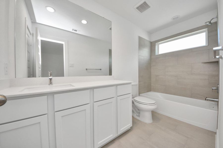 Secondary bath features tile flooring, bath/shower combo with tile surround, light stained wood cabinets, beautiful light countertop.