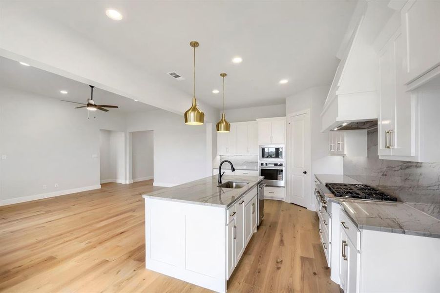 Open-concept kitchen featuring white cabinetry, light-toned wood-finish flooring, and integrated stainless-steel appliances