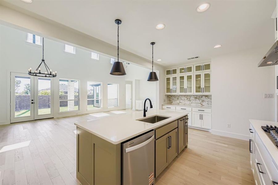 Kitchen with appliances with stainless steel finishes, light wood finished floors, white cabinets, glass insert cabinets, and recessed lighting Kitchen with appliances with stainless steel finishes, light wood finished floors, white cabinets, glass insert cabinets, and recessed lighting