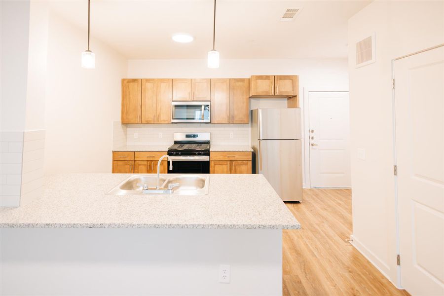 Kitchen featuring appliances with stainless steel finishes, a peninsula, light wood-type flooring, backsplash, and decorative light fixtures