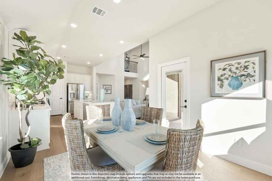 Bright dining area with wicker chairs and wood table, open to white kitchen with stainless appliances and hardwood floors