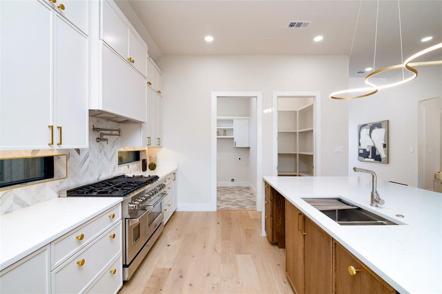 Kitchen with sink, light hardwood / wood-style floors, decorative light fixtures, range with two ovens, and white cabinets