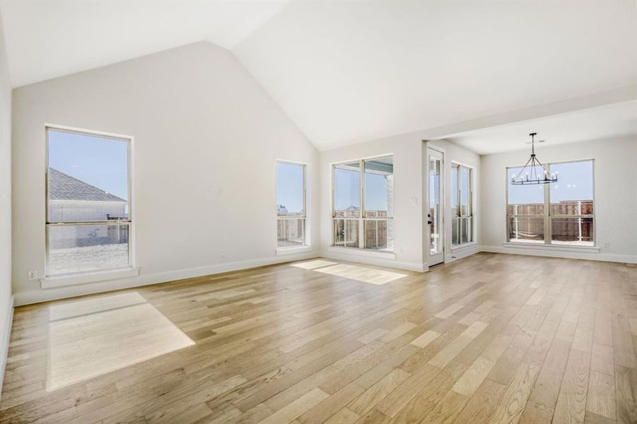 Unfurnished living room featuring hanging lights, light wood-style flooring, and a high ceiling