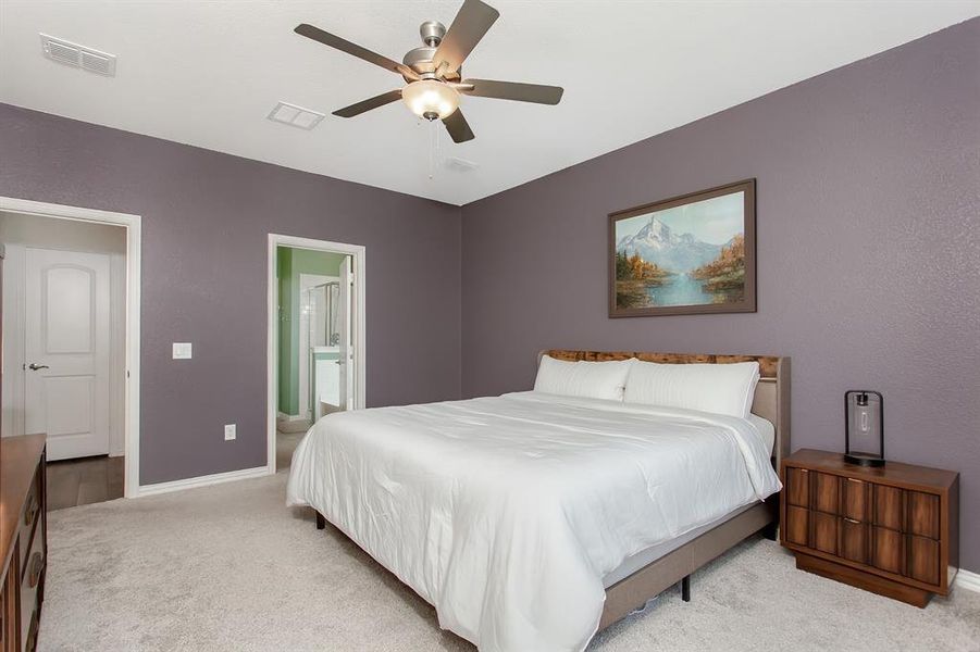 Bedroom featuring light carpet, ensuite bathroom, and a ceiling fan
