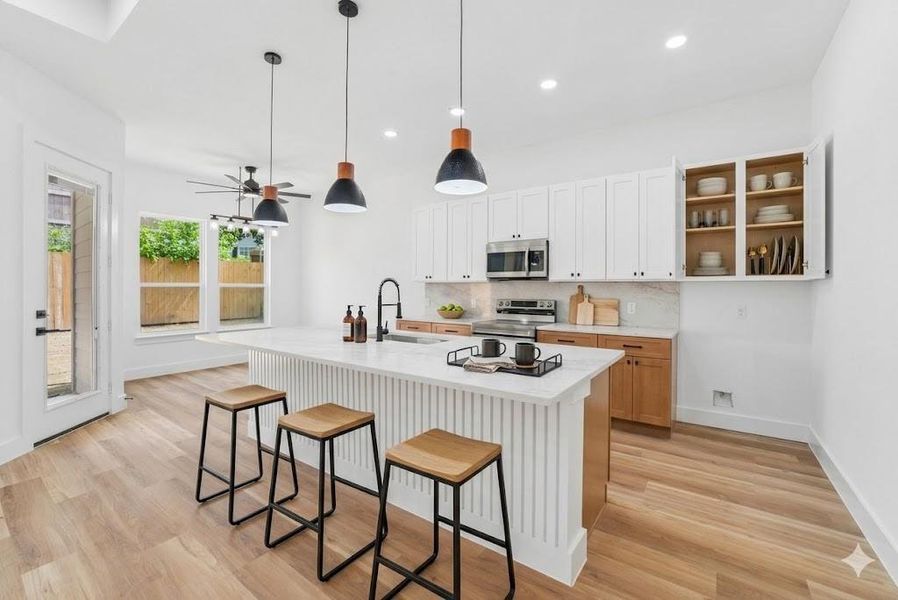 Virtually Staged - Contemporary kitchen featuring a large central island with a waterfall countertop, white shaker-style upper cabinetry, and stainless steel appliances Virtually Staged - Contemporary kitchen featuring a large central island with a waterfall countertop, white shaker-style upper cabinetry, and stainless steel appliances
