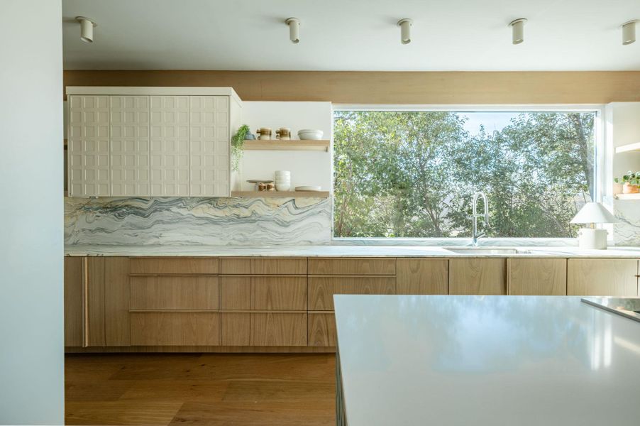 Kitchen featuring open shelves, wood finished floors, and light stone counters