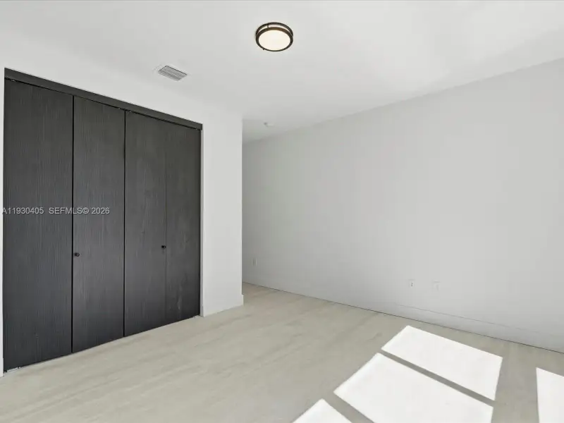 Interior space featuring light-toned wood-finish flooring, charcoal-toned floor-to-ceiling closet doors with knob hardware, and a circular flush-mount ceiling light fixture Interior space featuring light-toned wood-finish flooring, charcoal-toned floor-to-ceiling closet doors with knob hardware, and a circular flush-mount ceiling light fixture
