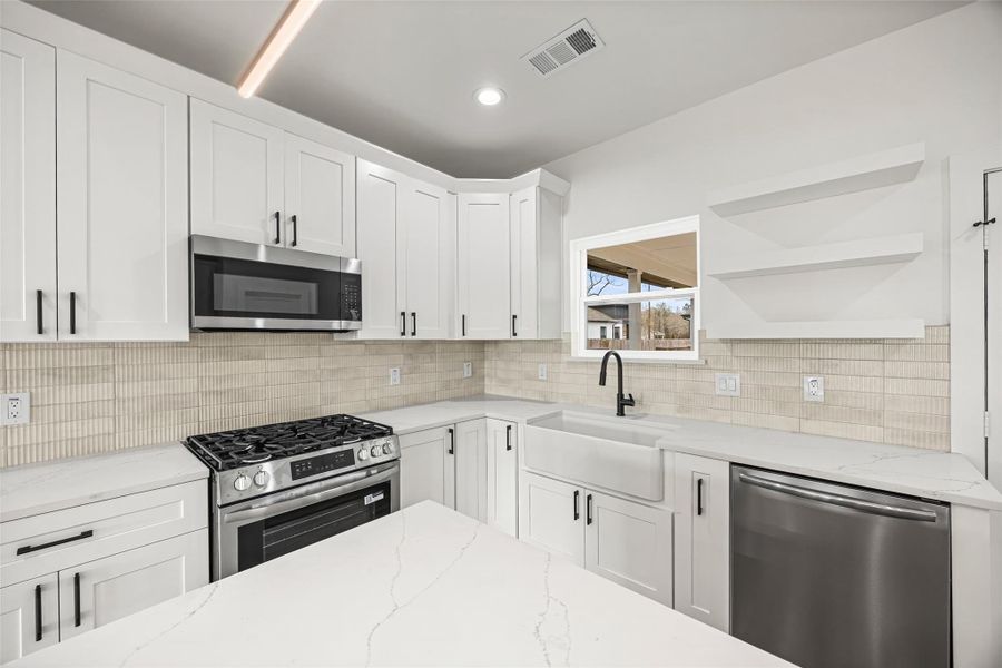 Shaker-style cabinetry, quartz countertops, stainless steel gas range, built-in microwave, and textured tile backsplash.