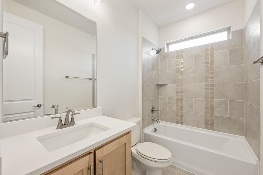 Bathroom with wood vanity, white countertop, and tiled tub-shower combo with small window above