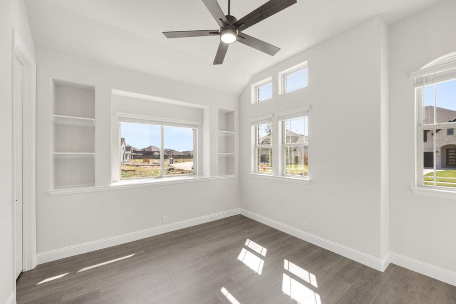 Empty room with vaulted ceiling, ceiling fan, built-in shelves, and hardwood floors Empty room with vaulted ceiling, ceiling fan, built-in shelves, and hardwood floors