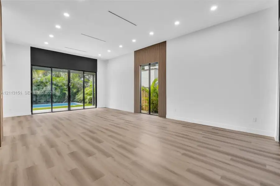 Open-concept interior featuring wood-finish flooring, recessed lighting, expansive glass sliding doors, and wood-paneled accent wall detailing Open-concept interior featuring wood-finish flooring, recessed lighting, expansive glass sliding doors, and wood-paneled accent wall detailing