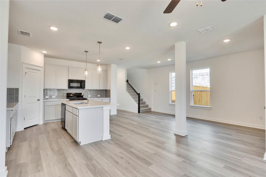 Kitchen featuring backsplash, an island with sink, open floor plan, pendant lighting, and light wood-style flooring