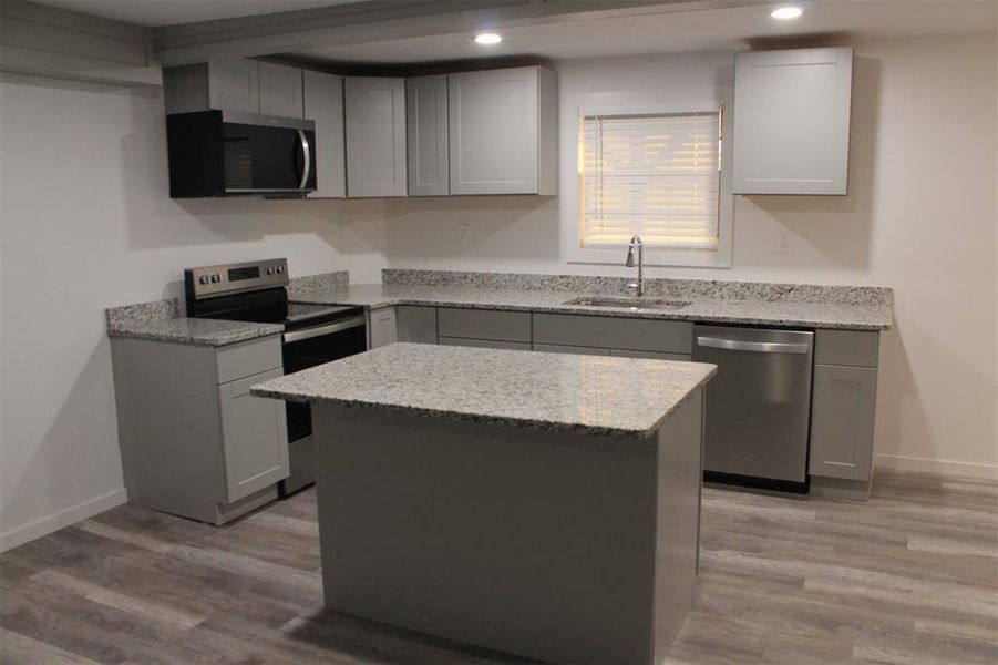 Kitchen featuring stainless steel appliances, gray cabinetry, light stone countertops, light wood-style floors, and recessed lighting