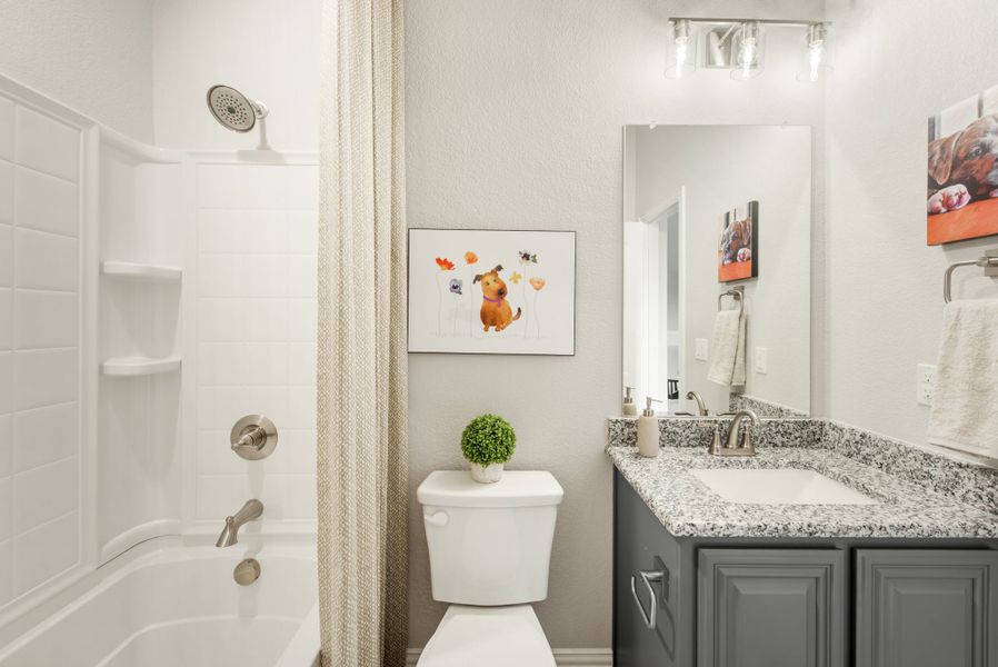 Bathroom with gray cabinets, granite countertop, single vanity, and tub-shower combo with white tile surround