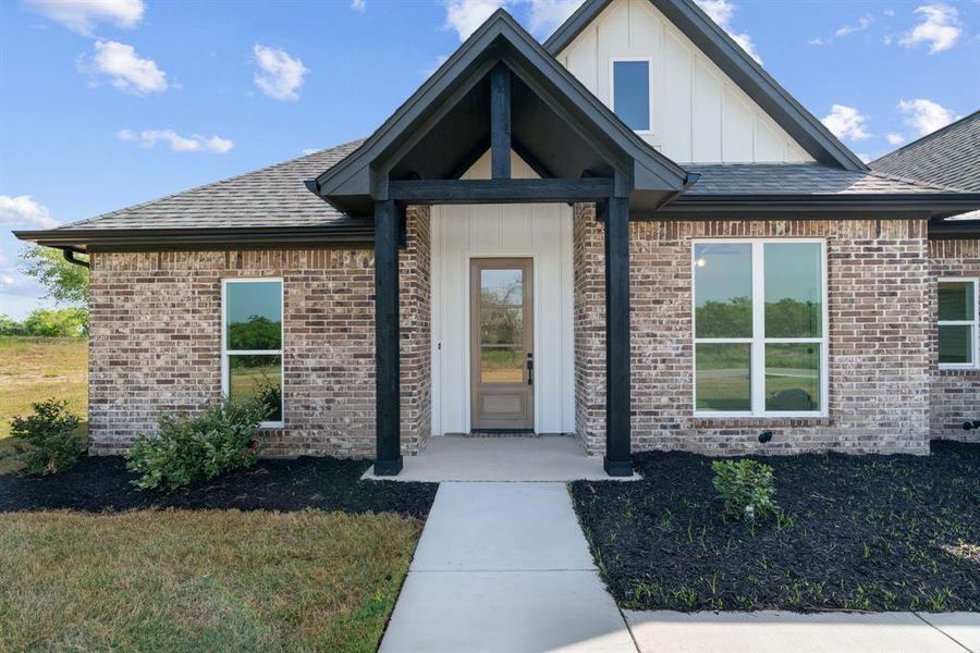 View of side of property featuring board and batten siding, brick siding, a lawn, and roof with shingles