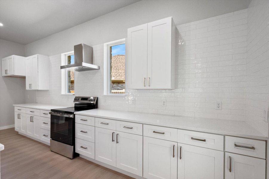 A well-appointed kitchen features pristine white cabinetry, light countertops, and a modern range with a sleek hood.