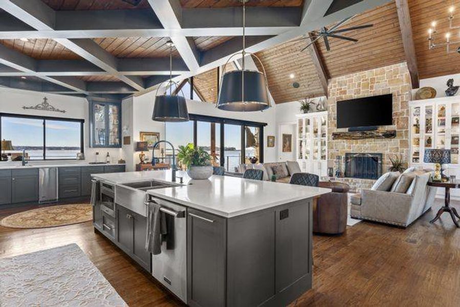 Kitchen featuring pendant lighting, a stone fireplace, a center island with sink, open floor plan, and dark wood finished floors