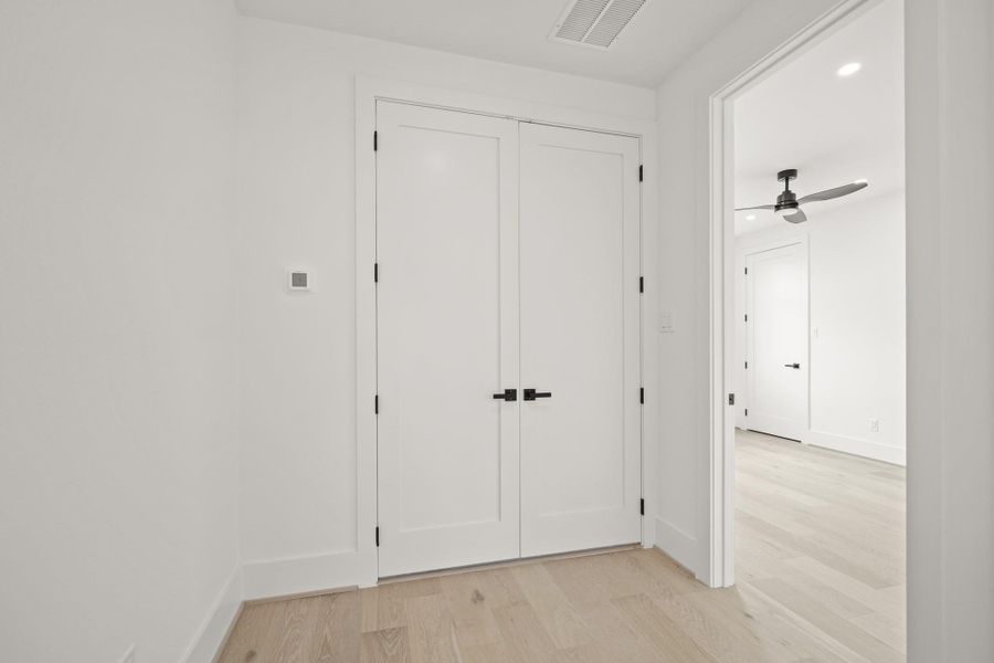 Double doors open to a laundry room with storage shelf and a hanging rod inside, all illuminated by recessed lighting above.