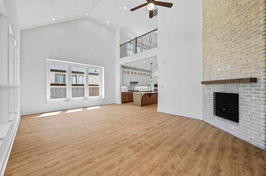 Unfurnished living room featuring a brick fireplace, high vaulted ceiling, light wood-type flooring, recessed lighting, and a ceiling fan Unfurnished living room featuring a brick fireplace, high vaulted ceiling, light wood-type flooring, recessed lighting, and a ceiling fan
