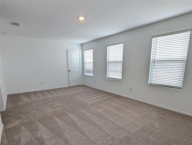 A spacious room offers plush carpet and ample natural illumination through multiple windows.