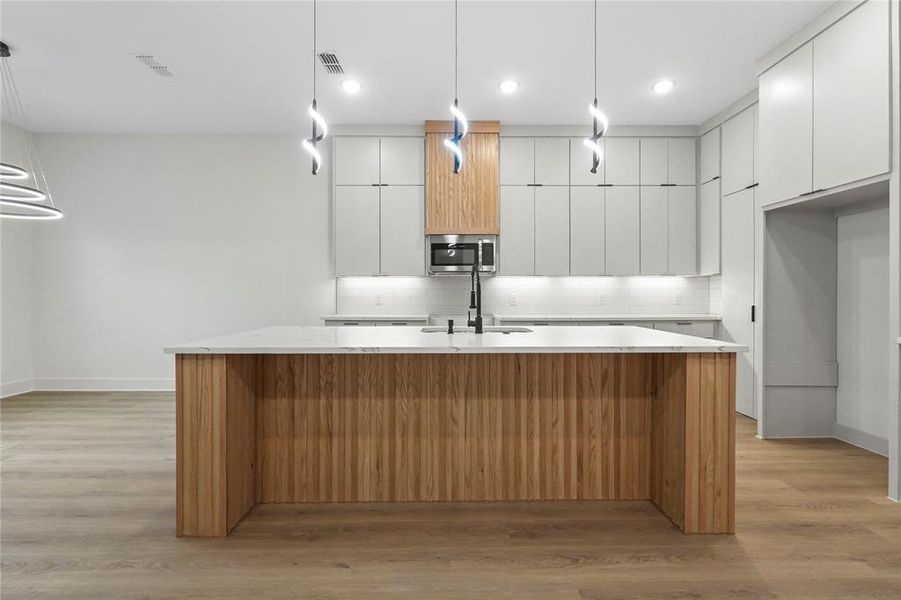Kitchen with modern cabinets, pendant lighting, white cabinets, light stone counters, and an island with sink