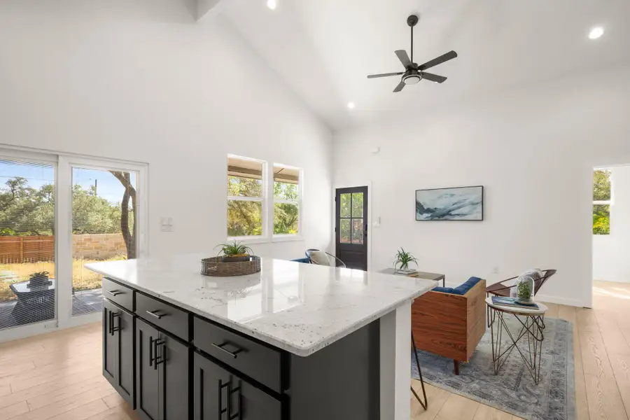 Kitchen featuring dark cabinetry, light wood finished floors, light stone countertops, high vaulted ceiling, and a kitchen island