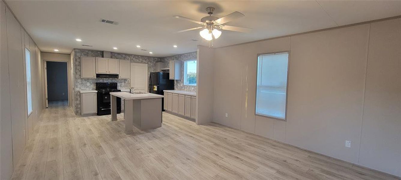 Kitchen with under cabinet range hood, visible vents, black appliances, and light wood-style floors