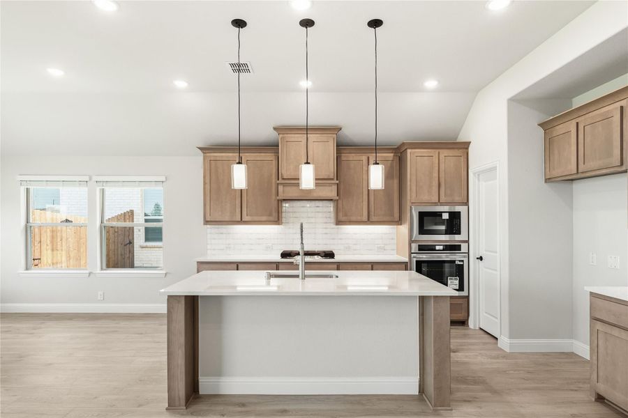 Kitchen with center island, tan wood cabinets, white countertops, pendant lights, and stainless steel appliances