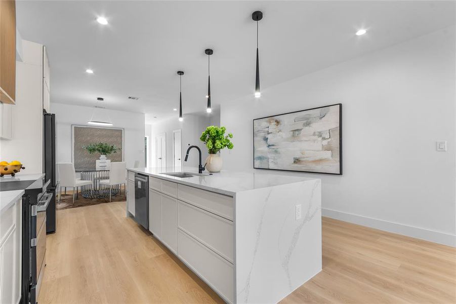 Contemporary kitchen featuring a spacious island with a waterfall countertop, integrated dishwasher, and under-mount sink with a matte black faucet Contemporary kitchen featuring a spacious island with a waterfall countertop, integrated dishwasher, and under-mount sink with a matte black faucet