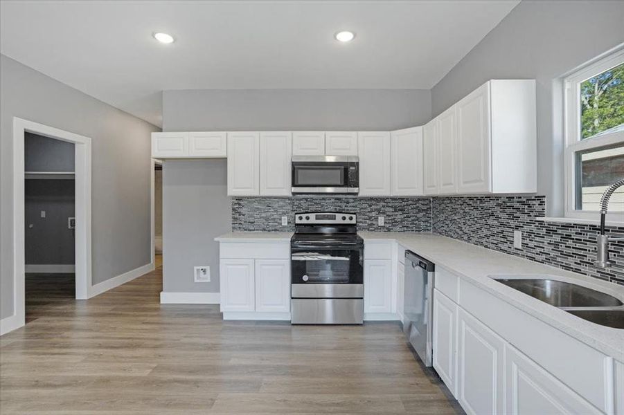 Kitchen with white cabinets, sink, appliances with stainless steel finishes, and light hardwood / wood-style floors