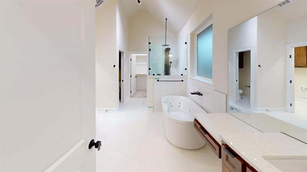 Full bath featuring a jetted tub, walk in shower, vanity, vaulted ceiling, and tile patterned floors