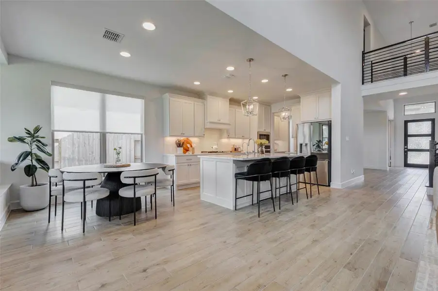 This spacious, modern kitchen features white cabinetry, a large island with seating, and stainless steel appliances. It's open to a bright dining area with large windows, and the space flows into a living area with high ceilings and contemporary finishes. This spacious, modern kitchen features white cabinetry, a large island with seating, and stainless steel appliances. It's open to a bright dining area with large windows, and the space flows into a living area with high ceilings and contemporary finishes.