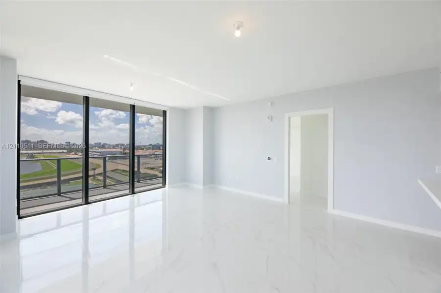 Open-concept interior featuring floor-to-ceiling glass windows, a private balcony with metal railing, and polished stone-finish tile flooring