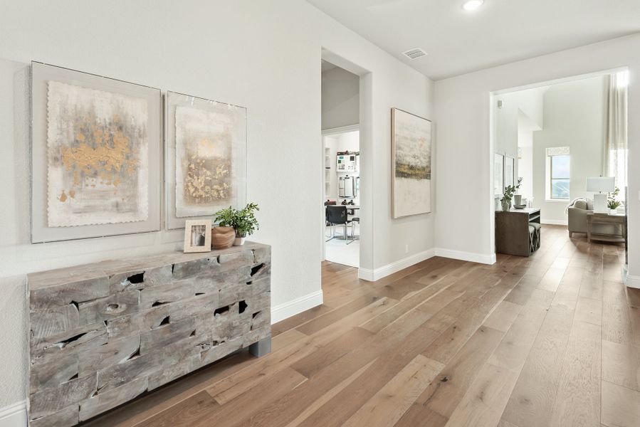 Bright hallway with hardwood floors, rustic wood console table, and framed wall art leading to open rooms