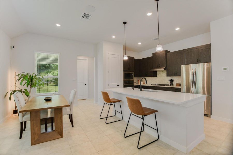 A contemporary kitchen and dining area features sleek dark cabinetry, stainless steel appliances, and a bright, functional island. A contemporary kitchen and dining area features sleek dark cabinetry, stainless steel appliances, and a bright, functional island.
