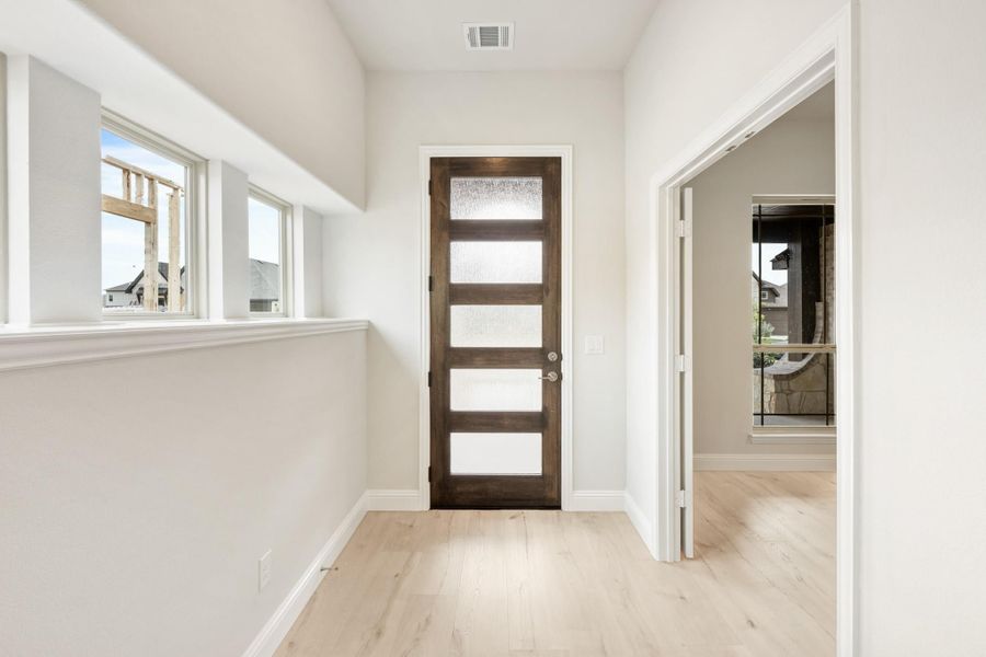 Hallway with dark wood glass-panel door, light hardwood floors, and white walls with clerestory windows