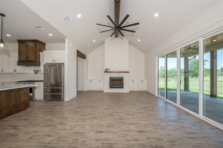 Unfurnished living room with a fireplace with raised hearth, a ceiling fan, wood tiled floors, recessed lighting, and high vaulted ceiling