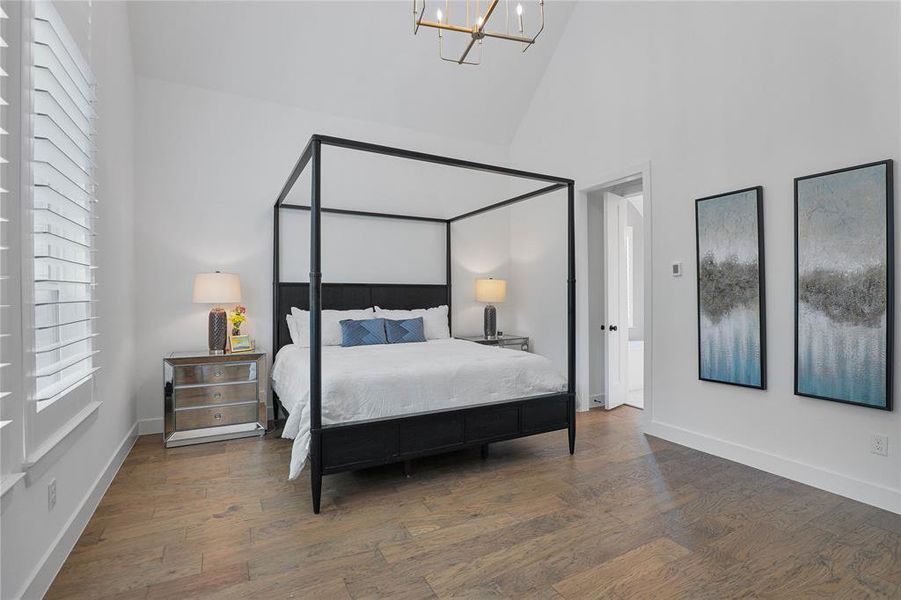 Spacious bedroom featuring vaulted ceilings, wood-finish flooring, white plantation shutters, and a contemporary chandelier